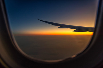 Naklejka premium Skrzydło sylwetki samolotu w widoku wschód słońca przez okno.