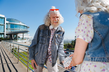 Elderly couple. Cheerful aged man looking at his wife while standing with her on the bridge