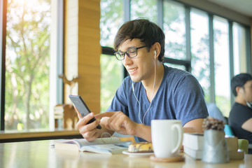 Young man texting message on smart phone while listening to music on earphones and enjoying free wireless internet connection at coffee shop