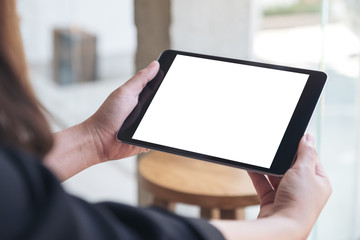 Mockup image of a woman holding black tablet pc with blank white desktop screen in cafe