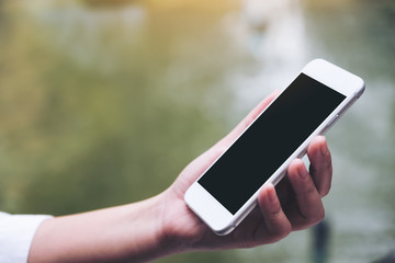 Mockup image of a woman holding white smart phone with blank black desktop screen with blur green nature background
