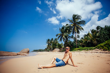 Man relaxing on a tropical beach. Young tanned man taking sunbath on sand beach with many palm trees. Enjoy and relax vacation concept