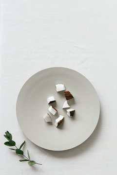 A collection of coconut bites on a neutral plate seen from above on a white surface.