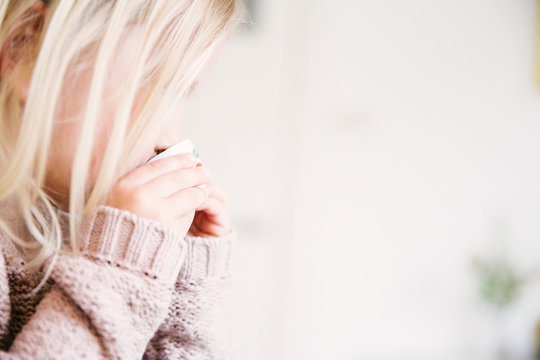 A blonde toddler girl wearing light pink knitwear is pretend drinking from her little miniature china tea set.