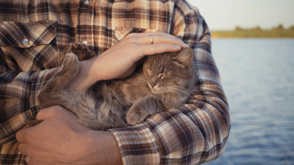 young guy stroking a cat on the nature near the lake.