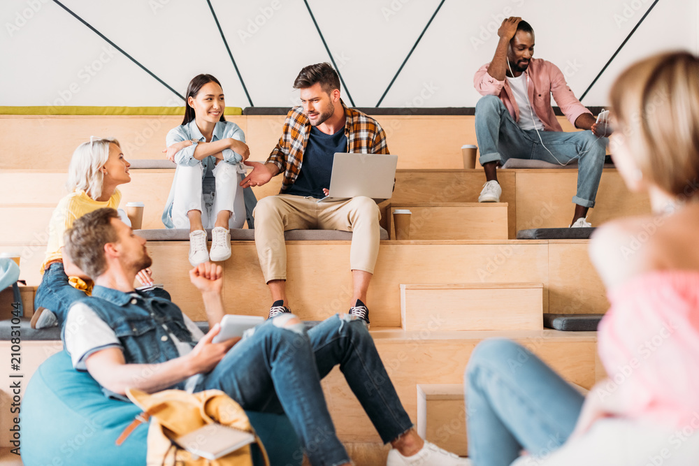 Wall mural happy young students spending time together at college on wooden tribunes