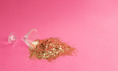 Spilled martini glass full of gold glitter on pink background. Creative minimal party concept.