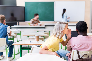Obraz premium rear view of young students gossiping at classroom during lesson