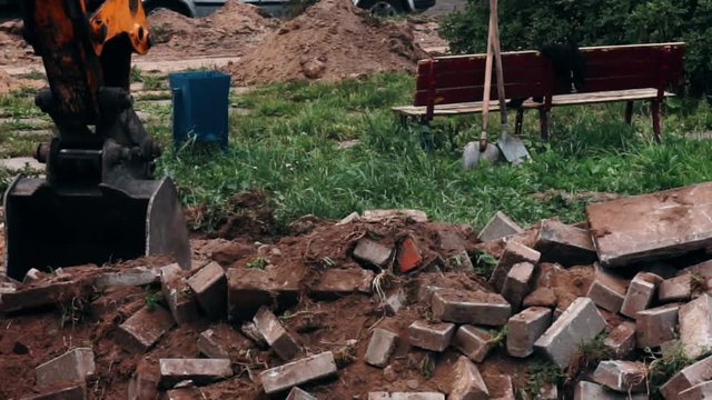 excavator bucket destroys the old road out of bricks.close-up