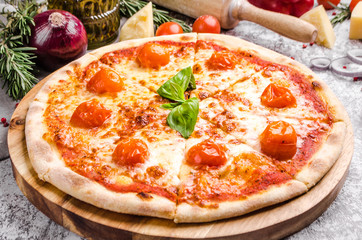 Homemade Meat Loves Pizza with basil, cherry tomatoes, pepperoni sausage, bacon, onions, cucumber, cheese on a wooden board over stone table background, restaurant menu concept. Italian food style