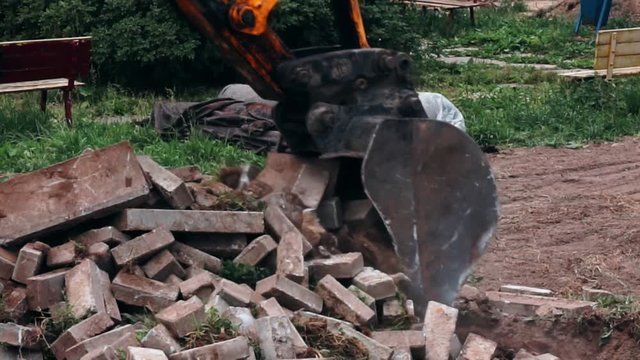 excavator bucket destroys the old road out of bricks.close-up