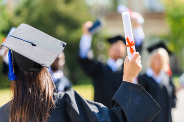 rear view of graduated student girl with diploma greeting classmates
