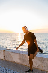 handsome adult sportsman in headphones stretching before training on seashore
