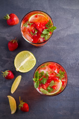 Strawberry mojito cocktail with berries, lime and mint. Summer berry cocktail on black background. overhead, vertical