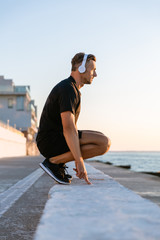 side view of handsome adult sportsman in headphones standing squats on parapet on seashore