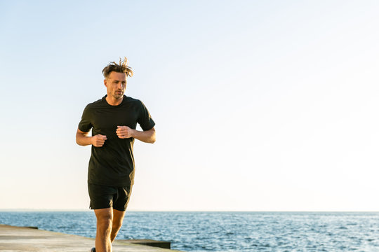 athletic adult joger running on seashore in morning