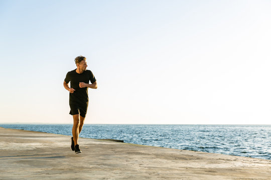 sporty adult joger running on seashore in morning