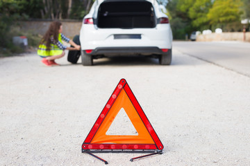 The woman has broken the car she is trying to change the wheel