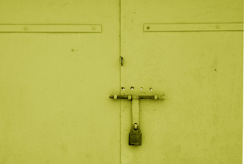 Old padlock on metal gate in yellow color.