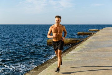 muscular shirtless sportsman jogging on seashore
