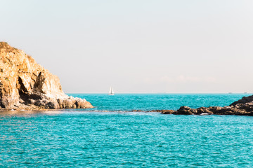 Two small rock islands in open sea connected with narrow isthmus. Lonely sailing boat with white sails . Beautiful romantic landscape, seascape. Natural background with copy space.