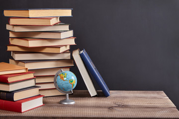 A pile of books with globe  on the table. Blackboard background with copy space. Education concept.
