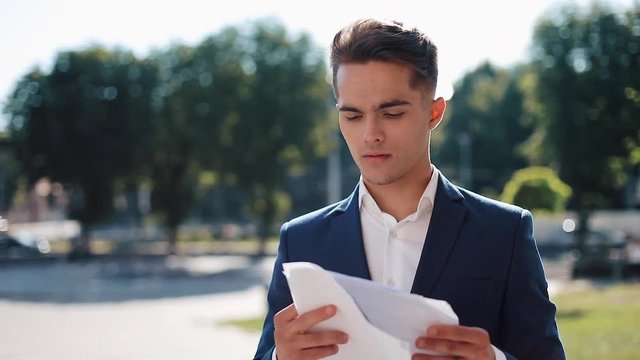 A serious young businessman in a stylish suit carefully examines the papers. Successful lifestyle, contract, responsibility