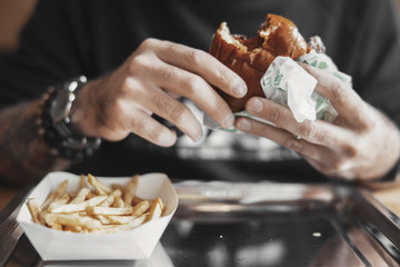 Young bearded man eating burger and french fries close up.