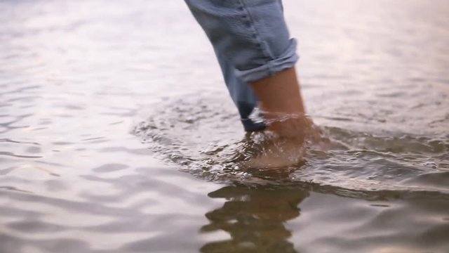 Close up footage of a young woman's feet walking by water, lake in blue jeans. Daytime, summer