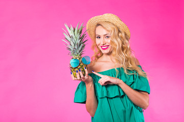 Happy young woman holding a pineapple on a pink background. Summer, diet and holidays concept