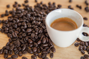 A cup of espresso on coffee beans on wooden table.