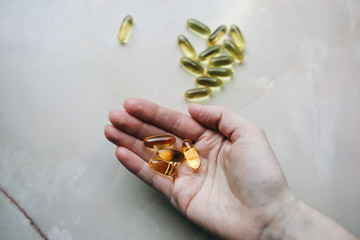 Omega 3 pills in woman's hand on marble background. Healthy diet supplements. Fish oils for vegans...
