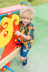 high angle view of happy curly boy riding on rocking horse at playground
