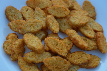 On white glass plate, crumbs of sliced dry baguette with taste and aroma, tomato and greens