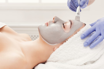 Naklejka premium Woman gets face mask by beautician at spa