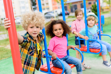 Fototapeta na wymiar multicultural group of little children riding on swings at playground