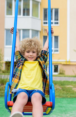 Fototapeta na wymiar happy curly little boy riding on swing at playground