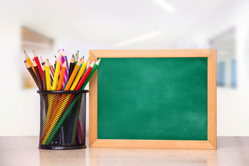 A glass with pencils and a school board for writing on a wooden table