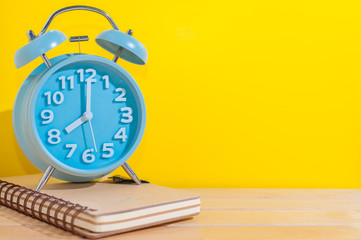 Blue analog alarm clock on wooden table with Yellow Background.