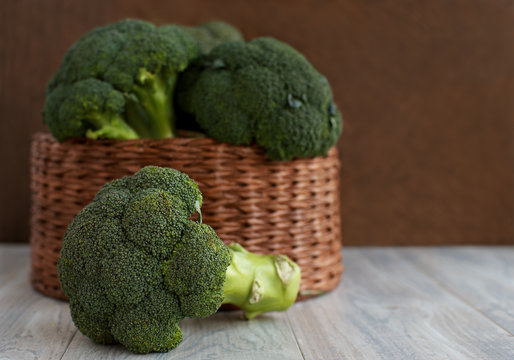 A lot of broccoli in a basket on a brown background. Large wicker basket with broccoli on a wooden background. Vegetables in the form of cabbage.