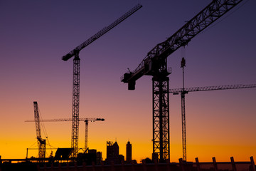 Silhouette cranes against a blue and orange sky