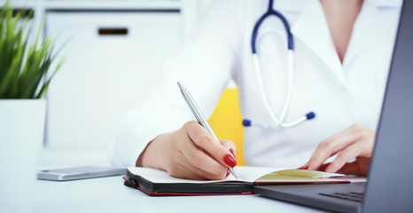Female medicine doctor hand holding silver pen writing something on clipboard and working laptop closeup. Physician ready to examine patient and help