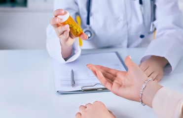 Female medicine doctor hand hold jar of pills and explain how to take pills to patient at...