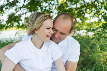 ouple in love. Man and woman in an embrace. A couple sitting in the grass in white T-shirts.
