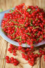 Red juicy currant lies on a wooden table and in plate.