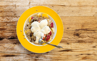 Müsli aus Obst und Samen mit Joghurt auf Teller mit gelbem Rand auf Holzuntergrund von oben