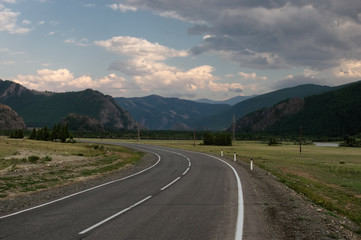 Naklejka premium Road asphalt path at the background of the high mountain ranges under a dark dramatic sky Altai Mountains Siberia, Russia