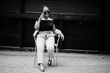 Fototapeta na wymiar Stylish african american woman in sunglasses posed outdoor at chair.