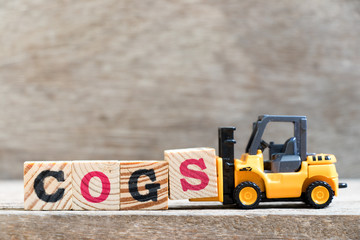 Toy forklift hold letter block S in word COGS (Abbreviation of Cost of goods sold) on wood background