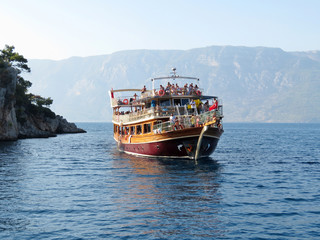 Boat with tourists under the Turkish flag sailing among the rocky islands of the Aegean sea. Summer excursions tour